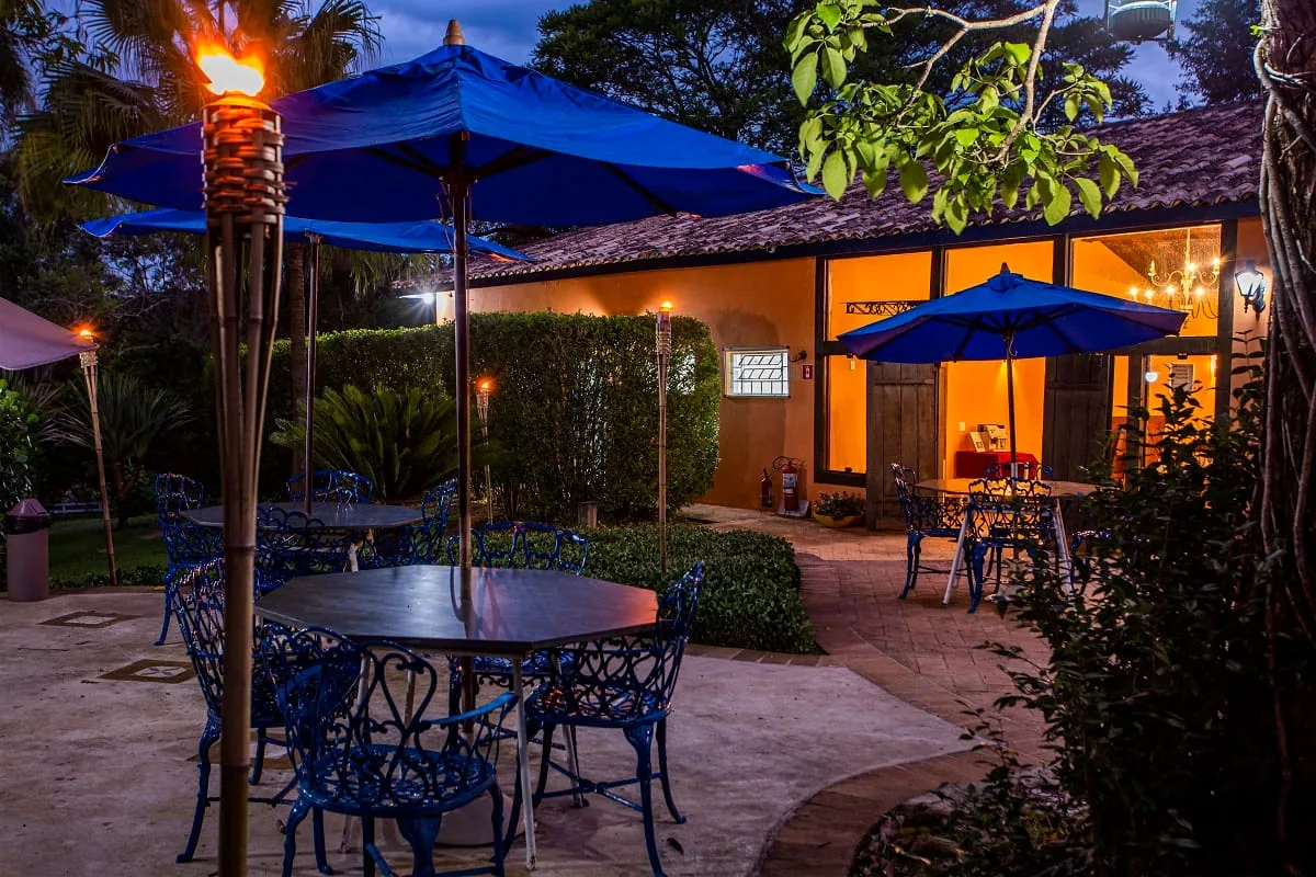 Terraço de mesas com guarda-sóis azuis ao anoitecer, iluminado por tochas