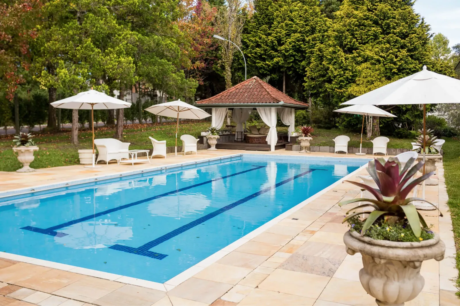 Piscina externa do Kurotel com guarda-sóis, espreguiçadeiras e gazebo entre as árvores