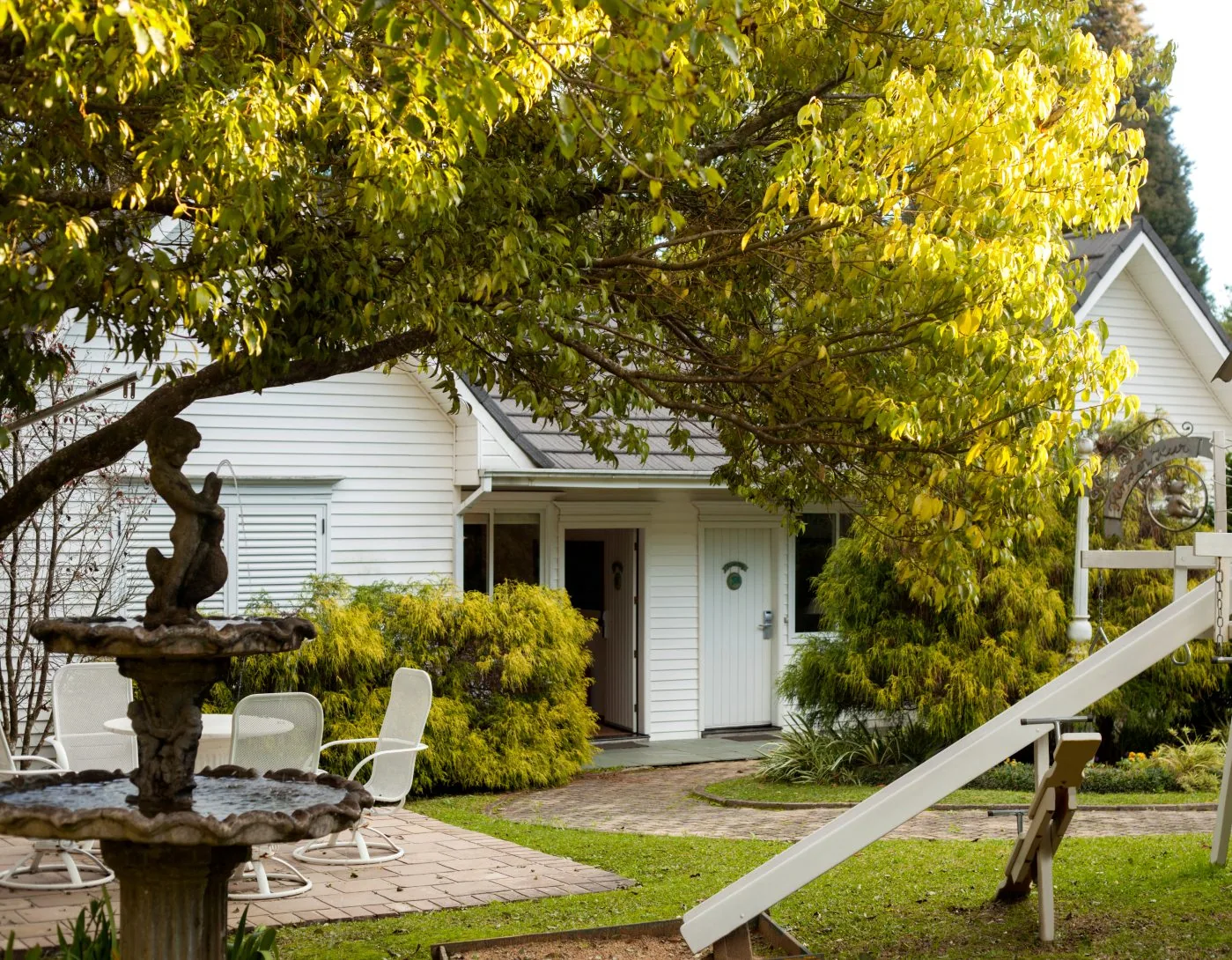 Chalé Kinder, casa branca entre as árvores, com chafariz e jardim