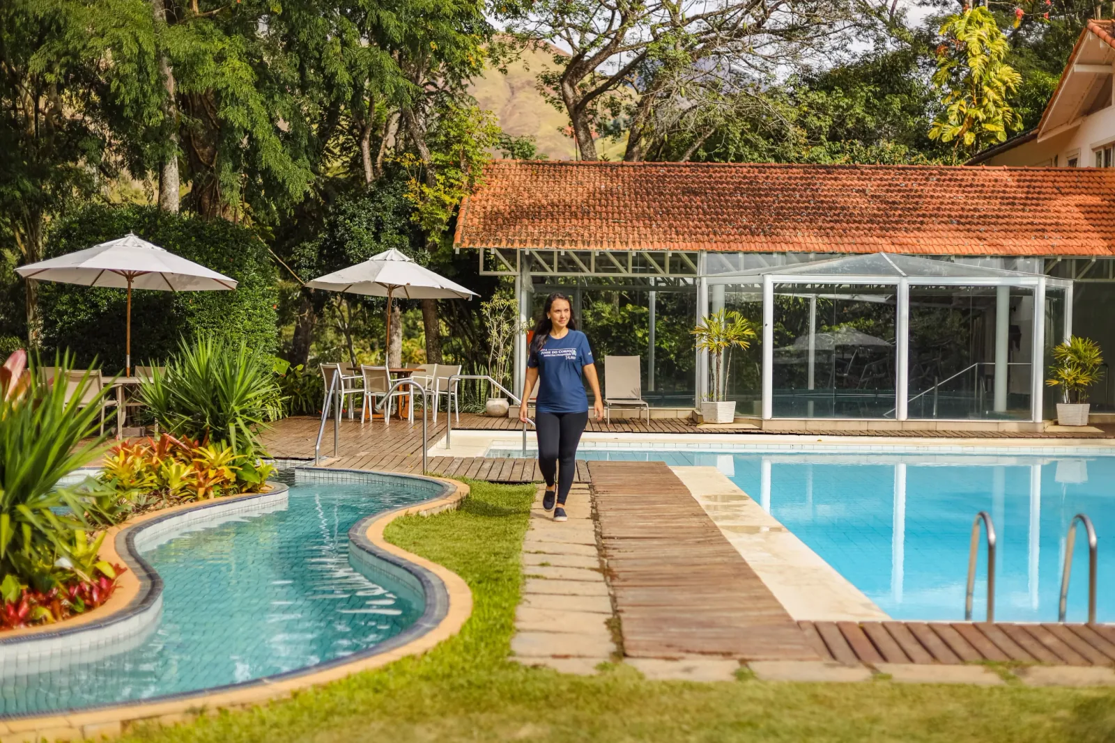 Piscina externa com guarda-sóis e o salão envidraçado ao fundo