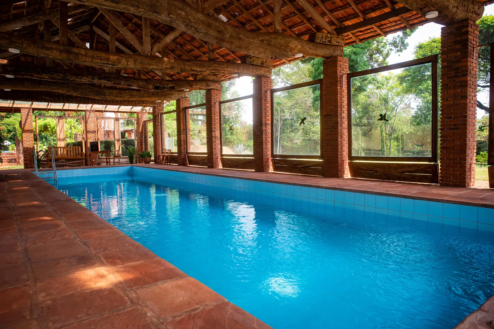 Piscina aquecida e coberta, com estrutura de madeira e janelões para a mata