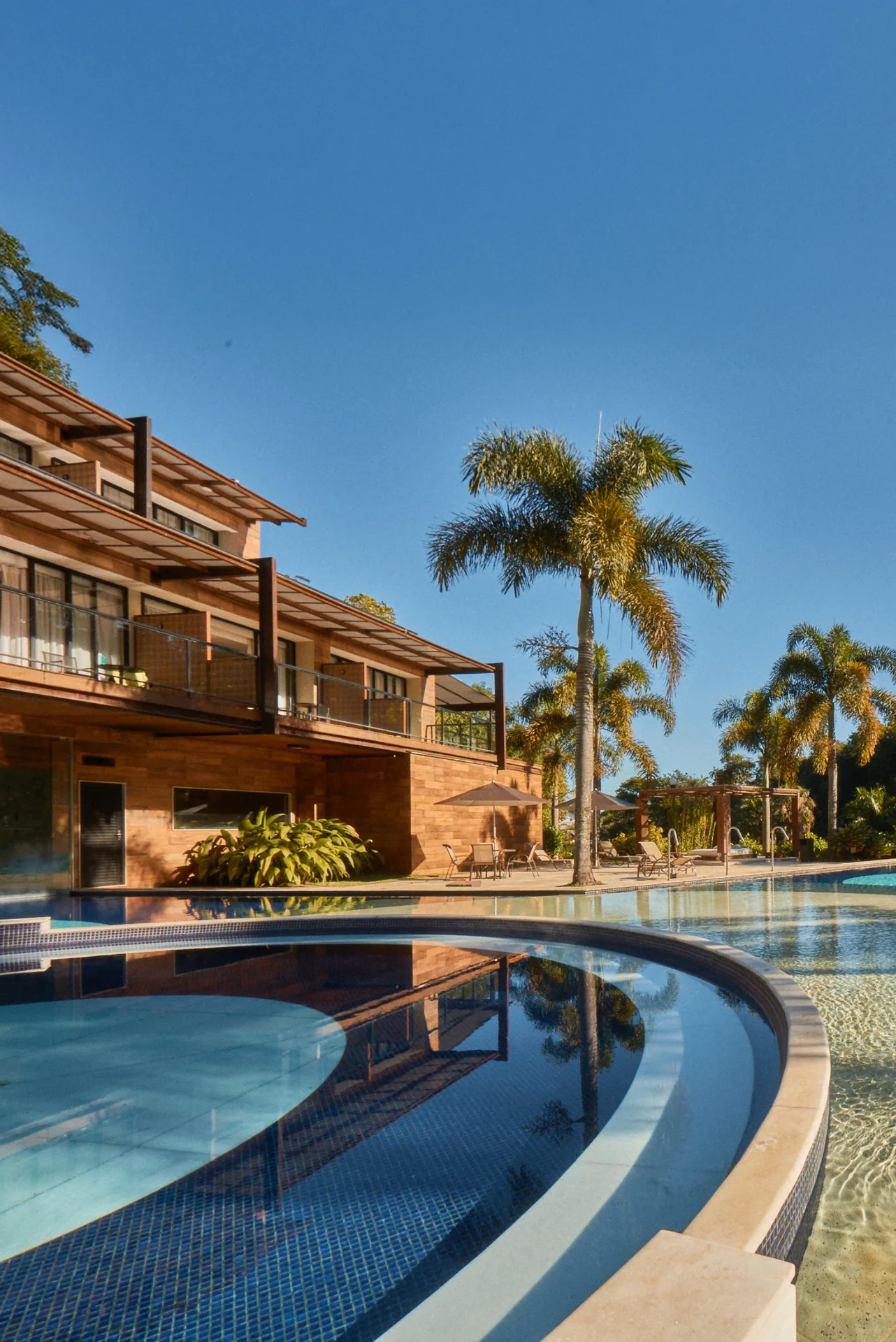 Prédio de apartamentos entre palmeiras, refletido na água da piscina