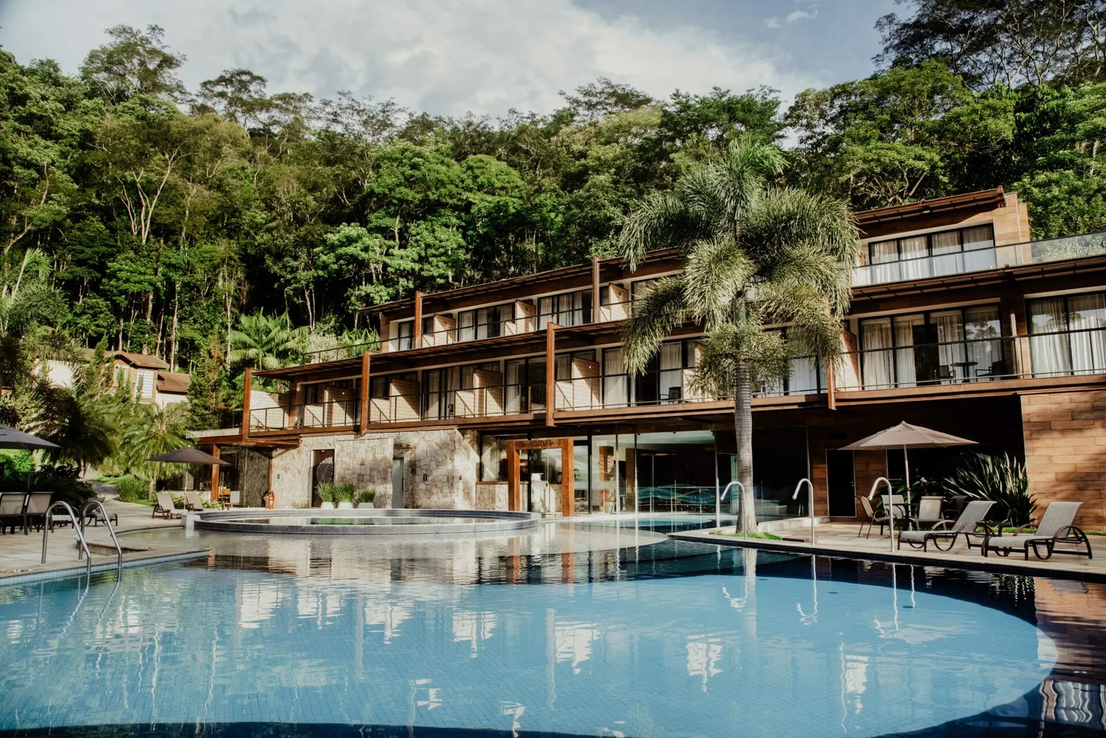 Piscina semiolímpica junto ao prédio, cercada de mata